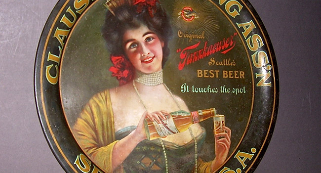 A round beer tray depicting a woman with dark hair wearing a formal gown and smiling as she pours beer from a bottle into a glass. There is small advertising text to the right of the woman.