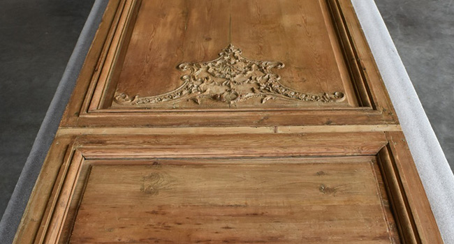 A tall, wide wood panel with carving laid out on a table during conservation treatment