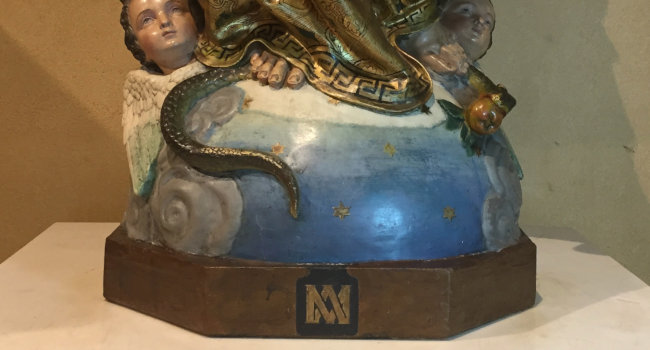 Base of a sculpture of the Virgin Mary on a heavenly blue sphere. Her foot is on the tail of a serpent and two cherub heads are visible.
