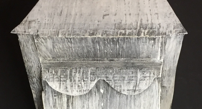An abstract geometric plaster sculpture. The sculpture is white with linear gray markings in the texture.